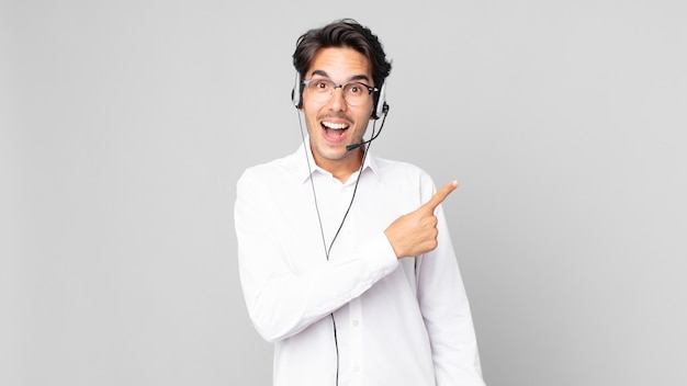 Young hispanic man looking excited and surprised pointing to the side. telemarketer concept