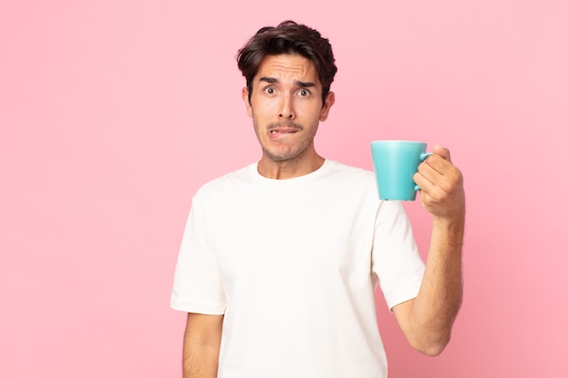 Young hispanic man looking puzzled and confused and holding a coffee mug