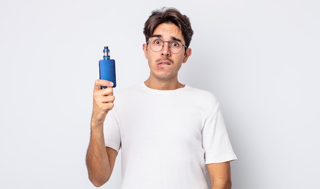 Young hispanic man looking puzzled and confused smoke vaporizer concept