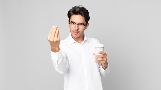 Young hispanic man making capice or money gesture, telling you to pay and holding a take away coffee