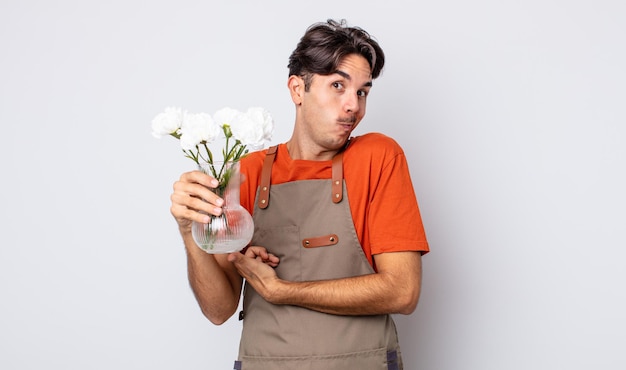 Photo young hispanic man shrugging, feeling confused and uncertain. florist concept