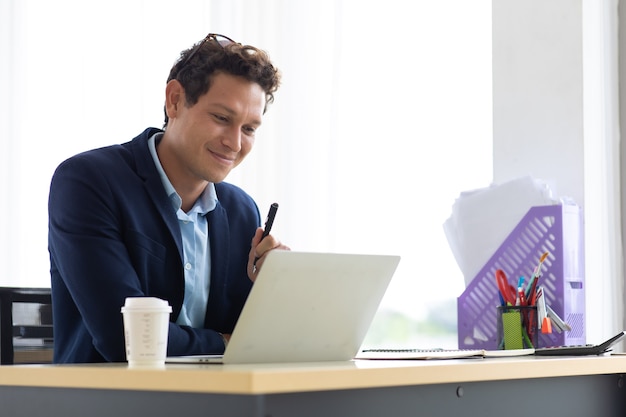 Young hispanic man sitting drink coffee and working on laptop computer at creative home office.