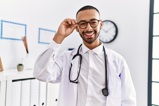 Young hispanic man smiling confident wearing doctor uniform at clinic