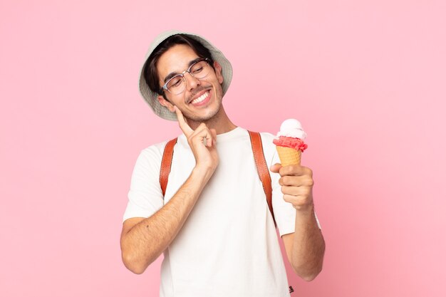 young hispanic man smiling happily and daydreaming or doubting and holding an ice cream