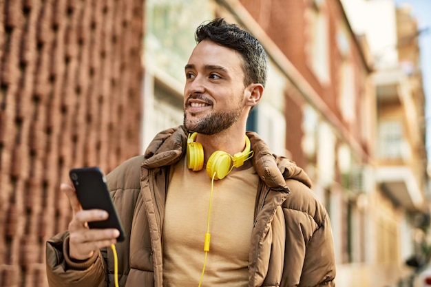 Young hispanic man smiling happy using smartphone and headphones at the city