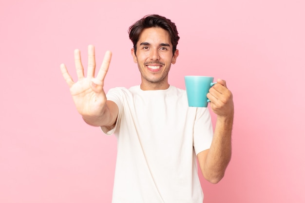 Young hispanic man smiling and looking friendly, showing number four and holding a coffee mug