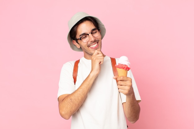 Young hispanic man smiling with a happy, confident expression with hand on chin and holding an ice cream