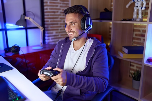 Young hispanic man streamer playing video game using joystick at gaming room