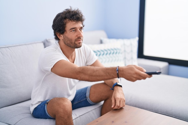 Young hispanic man watching movie sitting on sofa at home