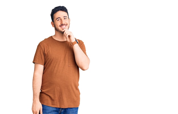 Young hispanic man wearing casual clothes looking confident at the camera with smile with crossed arms and hand raised on chin thinking positive