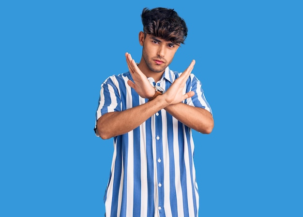 Young hispanic man wearing casual clothes rejection expression crossing arms doing negative sign, angry face