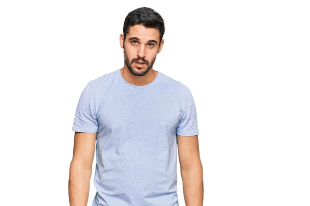 Young hispanic man wearing casual clothes in shock face looking skeptical and sarcastic surprised with open mouth