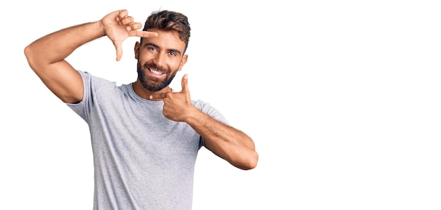 Young hispanic man wearing casual clothes smiling making frame with hands and fingers with happy face. creativity and photography concept.