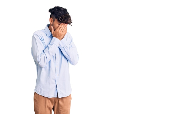 Young hispanic man wearing casual shirt with sad expression covering face with hands while crying depression concept