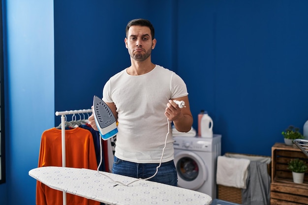 Young hispanic man with beard ironing clothes at home depressed and worry for distress crying angry and afraid sad expression