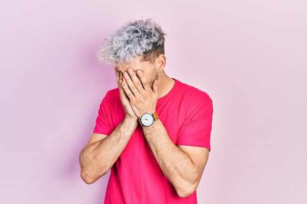 Young hispanic man with modern dyed hair wearing casual pink t shirt with sad expression covering face with hands while crying. depression concept.