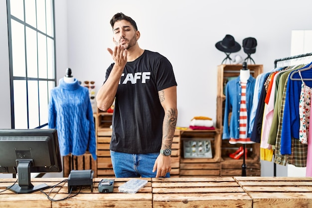 Young hispanic man working at retail boutique looking at the camera blowing a kiss with hand on air being lovely and sexy. love expression.