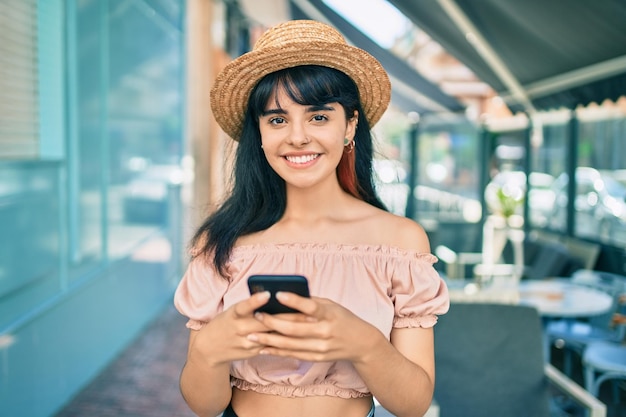 Young hispanic tourist girl wearing summer style using smartphone at the city