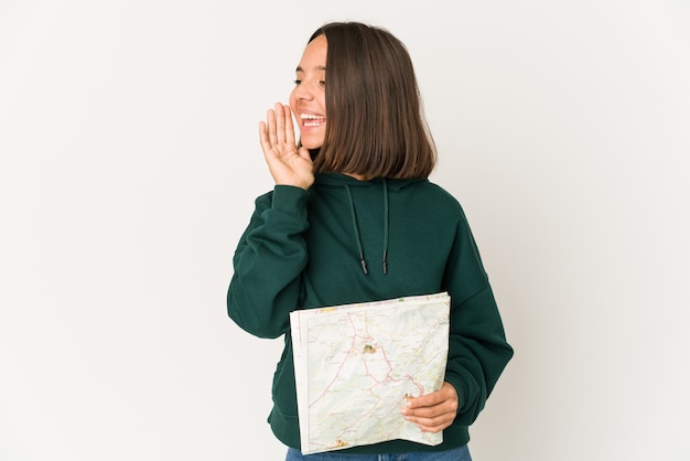 Young hispanic traveler woman holding a map shouting and holding palm near opened mouth.