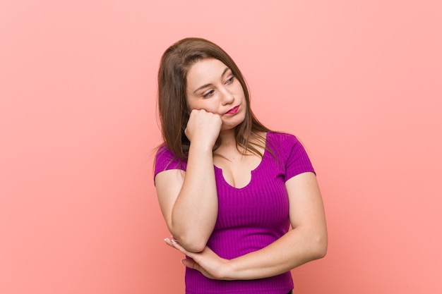 Young hispanic woman against a pink wall who feels sad and pensive, looking at copy space.