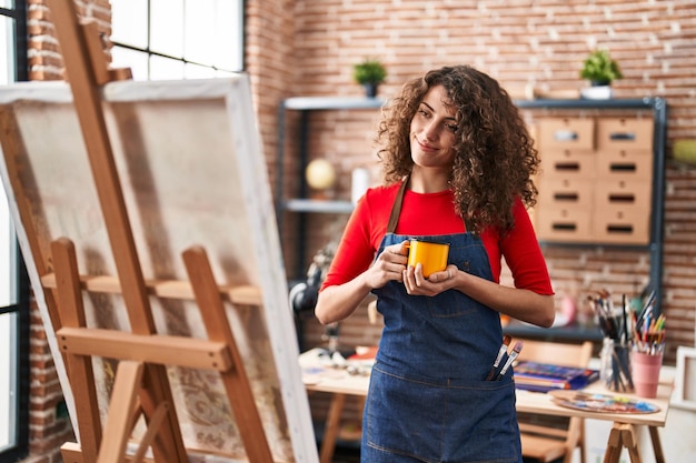 Young hispanic woman artist drinking coffee drawing at art studio