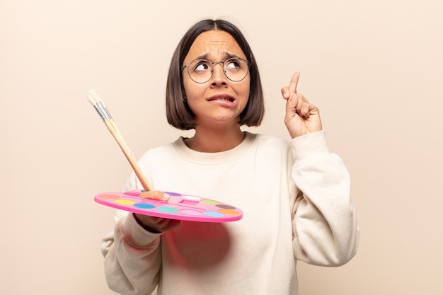 Young hispanic woman crossing fingers anxiously and hoping for good luck with a worried look