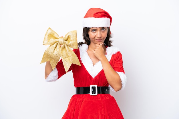 Young hispanic woman dressed as mama noel holding a Christmas bow isolated on white background thinking