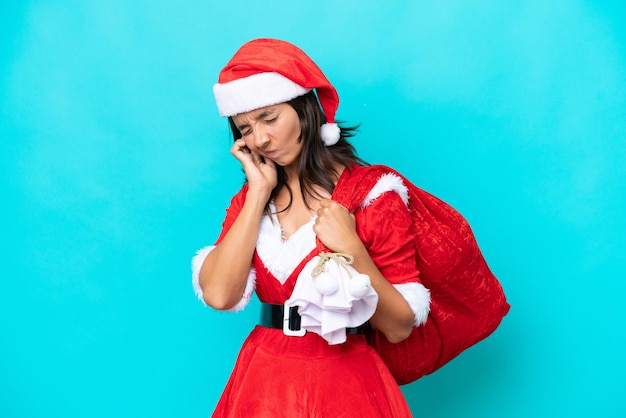 Young hispanic woman dressed as mama noel holding a sack isolated on blue background frustrated and covering ears