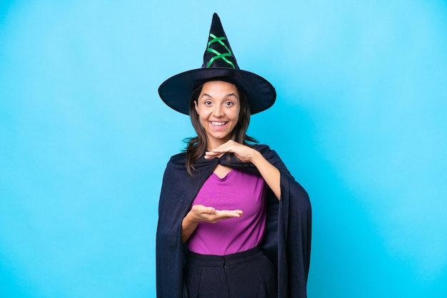 Young hispanic woman dressed as witch over isolated background holding copyspace imaginary on the palm to insert an ad