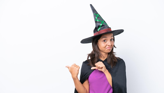 Young hispanic woman dressed as witch over isolated background pointing to the side to present a product