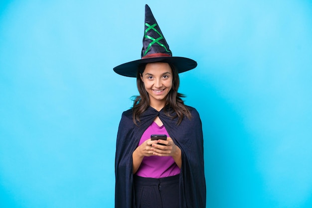 Young hispanic woman dressed as witch over isolated background sending a message with the mobile