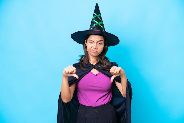 Young hispanic woman dressed as witch over isolated background showing thumb down with two hands