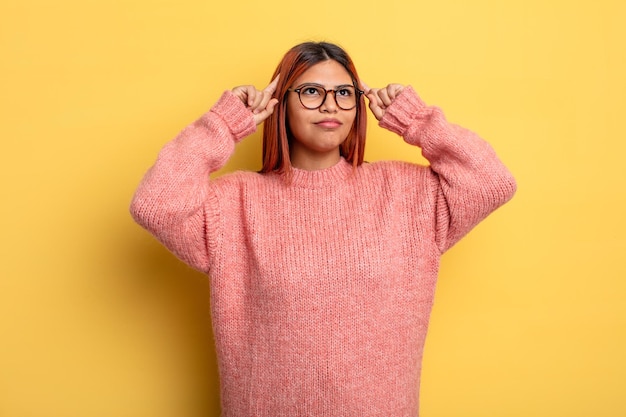 Young hispanic woman feeling confused or doubting, concentrating on an idea, thinking hard, looking to copy space on side