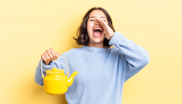 Young hispanic woman feeling happy,giving a big shout out with hands next to mouth. teapot concept