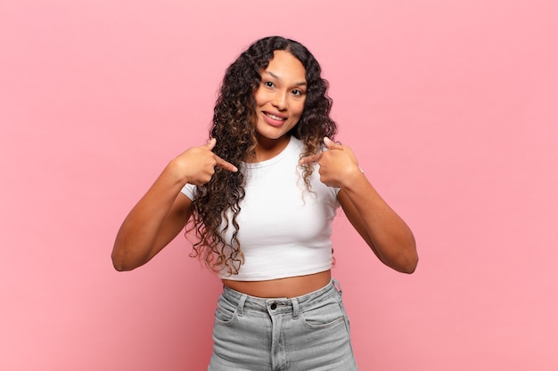 Young hispanic woman feeling happy, surprised and proud, pointing to self with an excited, amazed look