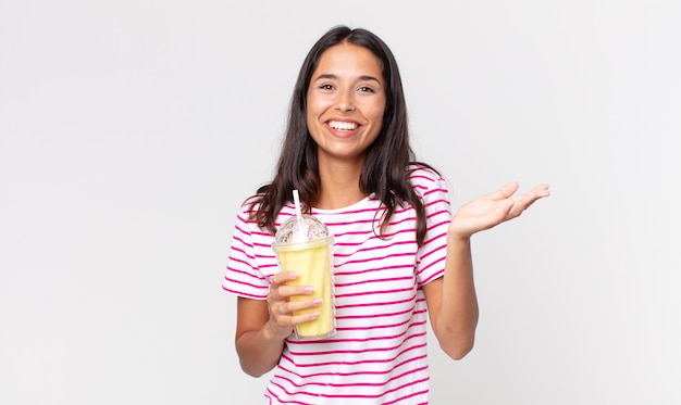 Young hispanic woman feeling happy, surprised realizing a solution or idea and holding a vanila smoothy milkshake