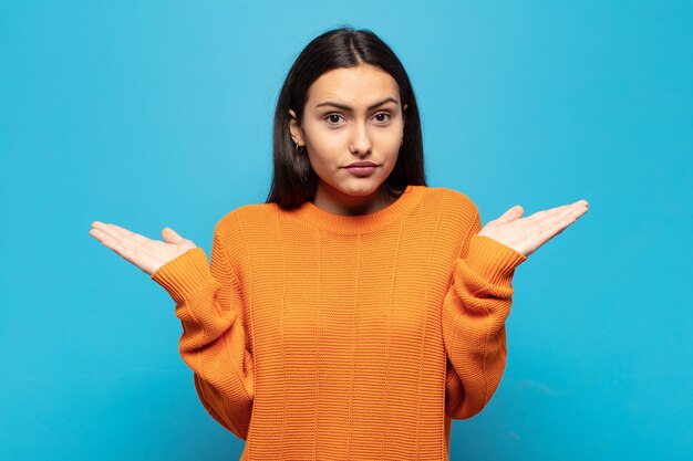 Young hispanic woman feeling puzzled and confused, doubting, weighting or choosing different options with funny expression