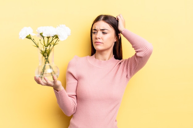 Young hispanic woman feeling puzzled and confused, scratching head. flower pot concept