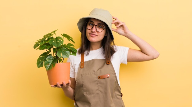 Young hispanic woman feeling puzzled and confused scratching head gardener and plant concept