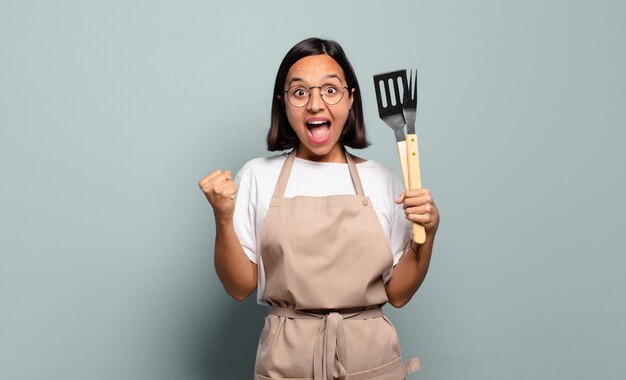 Young hispanic woman feeling shocked, excited and happy, laughing and celebrating success