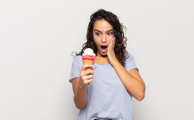 Young hispanic woman feeling shocked and scared, looking terrified with open mouth and hands on cheeks