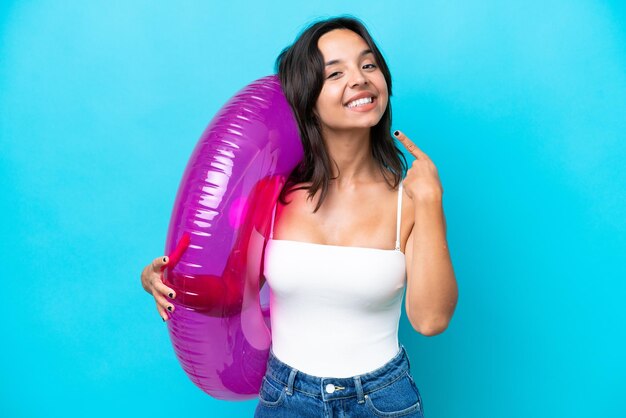 Young hispanic woman holding air mattress donut isolated on blue background giving a thumbs up gesture