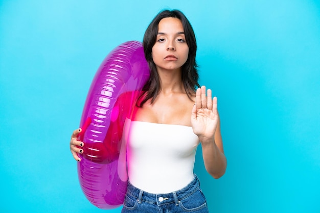 Young hispanic woman holding air mattress donut isolated on blue background making stop gesture