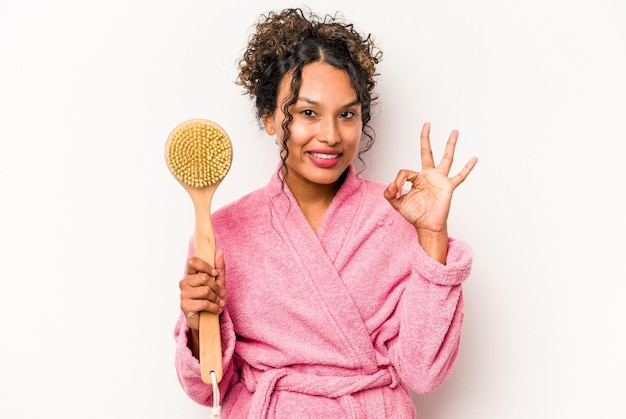 Young hispanic woman holding a back scratcher isolated on white background cheerful and confident showing ok gesture