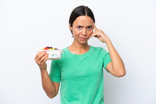 Young hispanic woman holding a bowl of fruit isolated on white background thinking an idea