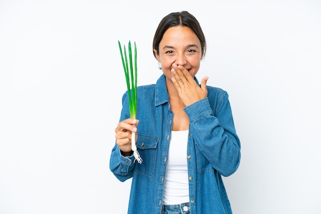 Young hispanic woman holding chive isolated on white background happy and smiling covering mouth with hand