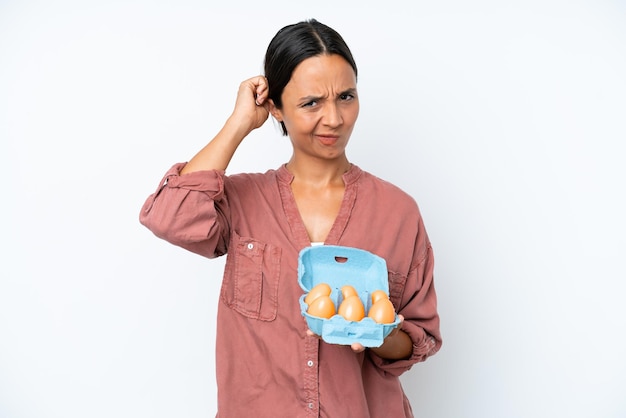 Young hispanic woman holding eggs isolated on white background having doubts