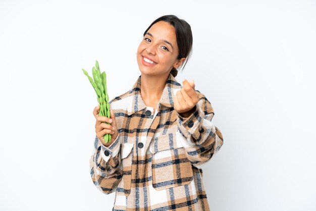 Young hispanic woman holding a green beans isolated on white background making money gesture