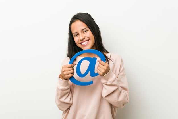 Young hispanic woman holding an at icon happy, smiling and cheerful.