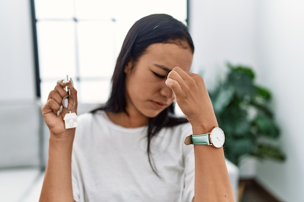 Young hispanic woman holding keys of new home tired rubbing nose and eyes feeling fatigue and headache stress and frustration concept